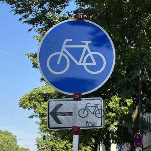 Ein Radwegschild mit kreativem Zusatzschild „Pfeil nach links + Fahrrad frei“.