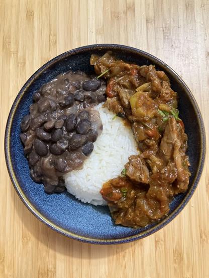 A shredded beef and tomato stew served with rice and black beans.