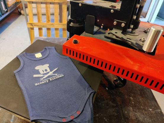 Baby Body in dunkelblau mit Binary Kitchen Logo und Aufschrift auf einer Siebdruckbank