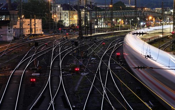 Es ist abends und dunkel: Blick auf ein Gleisfeld von einer Brücke, wobei die Schienen hell zu leuchten scheinen