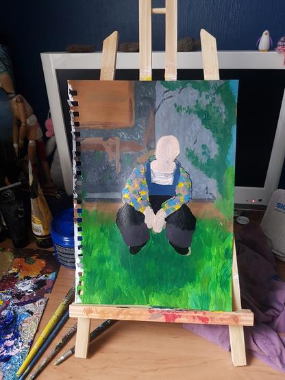 Peinture acrylique en cours d'une personne pour l'instant sans visage avec des vêtements colorés posant assise sur de l'herbe devant un atelier de bricolage