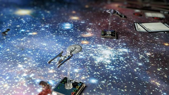 A closeup of a battle of a silver spaceship in the middle and a fleeing ship top middle..
There are a lot of stars on the table.
