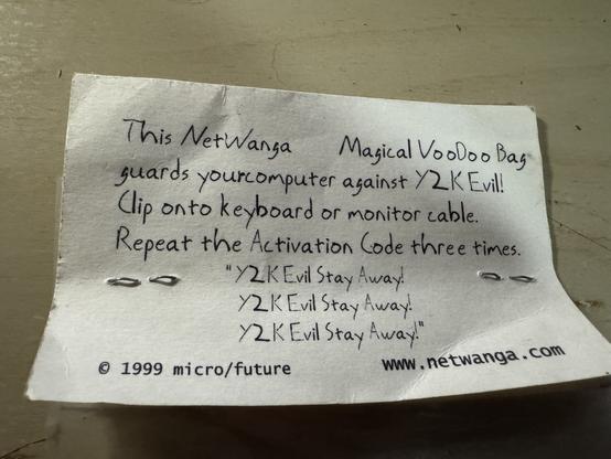 A close up of the card attached to a plastic bag. It has the following printed on it:  
This Netwanga Magical Voodoo Bag guards your computer against Y2K Evil! 
Clip onto keyboard or monitor cable.
Repeat the Activation Code three times.
“Y2K Evil Stay Away!
Y2K Evil Stay Away!
Y2K Evil Stay Away!”

Copyright Micro/future 
www.netwanga.com