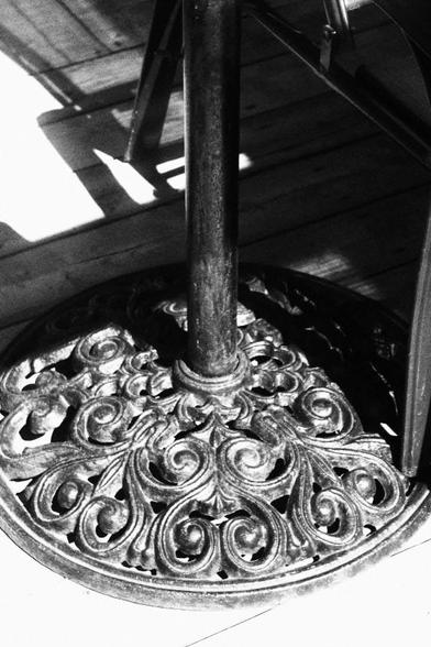 Medium close-up of the base of a wrought iron umbrella stand on a wooden deck.