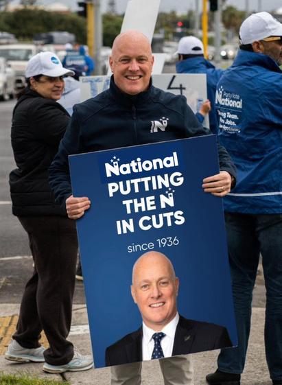Image is NZ Prime Minister Luxon holding a sign of himself which reads 
“National putting the N in cuts since 1936