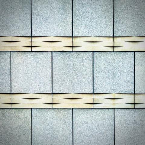 Rows of thin, tan, relief-staggered exterior wall sections vertically separate large, white squares speckled with blue flakes on an overcast day.