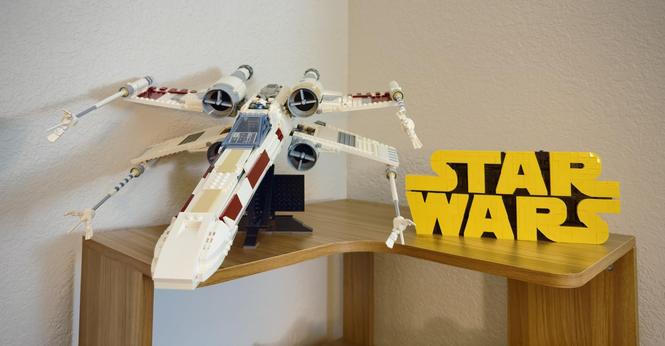 Lego X-Wing and Lego Star Wars logo against a white wall and on a light brown shelf.
