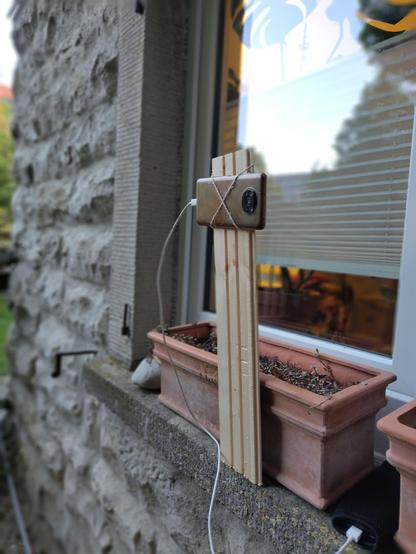 Eine provisorische Handyalterung an einem Brett das mit einem Eisenwinkel unter einem Pflanzkasten befestigt ist