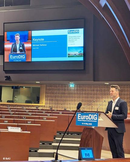 Michael Terhörst, Leiter der Stelle zur Durchsetzung von Kinderrechten in digitalen Diensten (KidD), bei seinem Vortag am 14.05.2025 zum Thema „Das Dilemma der Altersverifikation: Ausgleich zwischen Kinderschutz und digitalen Zugangsrechten“ auf dem #EuroDIG2025 in Straßburg am Council of Europe.

Die bei der Bundeszentrale für Kinder- und Jugendmedienschutz (BzKJ) eingerichtete unabhängige Stelle zur Durchsetzung von Kinderrechten in digitalen Diensten überwacht nach dem europäischen Digital Services Act, ob Anbieter von Online-Plattformen mit Sitz in Deutschland strukturelle Vorsorgemaßnahmen in ihren Angeboten eingerichtet haben. Dazu zählen etwa sichere Voreinstellungen, eine wirksame Altersüberprüfung sowie Melde- und Abhilfeverfahren.