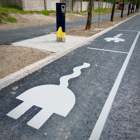 Parking spaces along a street depicted with electric plugs, and a charging station nearby.