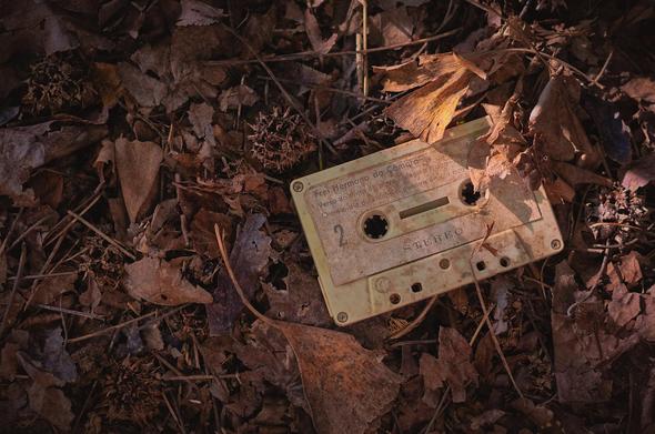 Foto de una cinta de cassette sucia y abandonada en el suelo entre hojas.