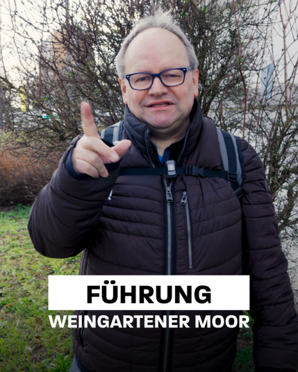 The image features a middle-aged man with short, graying hair and glasses, standing outdoors. He is wearing a dark puffer jacket and a backpack, and he is pointing directly at the camera with his right hand, making a gesture with his index finger. The background shows bare trees and grass, suggesting a park or natural area. The man has a friendly expression and is smiling slightly. Overlaid on the image is text in bold, white capital letters on a black background that reads "FÜHRUNG WEINGARTENER MOOR," indicating that the image is likely related to a guided tour of the Weingartener Moor.

Provided by @altbot, generated privately and locally using Ovis2-8B, edited