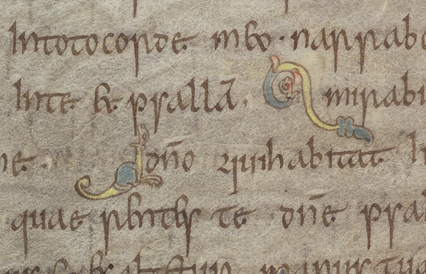 Five lines of medieval script in brown ink against a brownish-grey page, with two tiny yellow, green and pink hybrid creatures opening their mouths in the direction of letters.