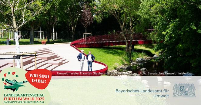 Zwei Männer stehen in einer Gartenanlage am Rande von amphietheaterartigen Stufen. Auf der anderen Seite schlängelt sich ein Bach entlang, frisch gepflanzte Bäume verweisen darauf, dass es sich um eine neue Anlage handelt, ein roter niedriger Zaun grenzt den Sitz- und Gehbereich vom Grün ab.