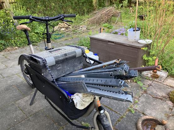 Photo of a Muli cargobike loaded with some scrap metal. The bike is situated in a garden and some metal rods are protruding from the bike’s cargo basket.