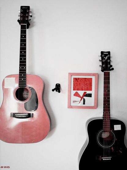 Farbfoto mit hervorgehobenen Rottönen und unterdrückten anderen Farben außer schwarz/weiß/grau, das einen Ausschnitt einer hellen Wand zeigt, an der zwei Gitarren und ein gerahmtes Bild hängen, auf dem im oberen Teil geschrieben steht "Rot ist schön".