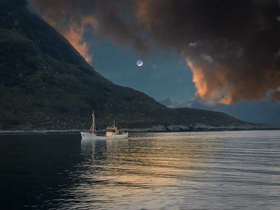 Ein weißes Schiff vor einem Berg im Sonnenuntergang