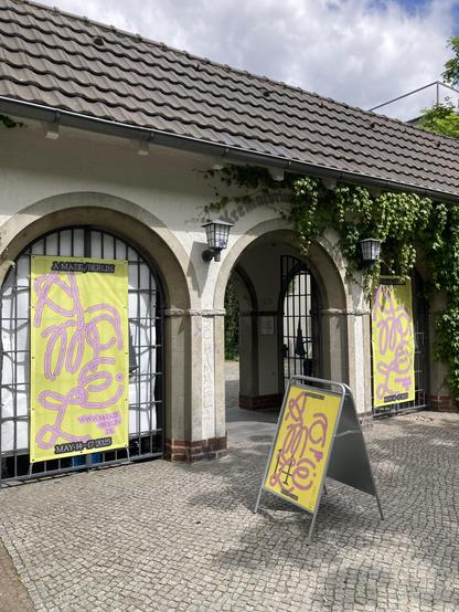 the entry arches to Amaze festival 2025 in Berlin Wedding, framed by the yellow festival posters. Blue sky, slightly cloudy, above.