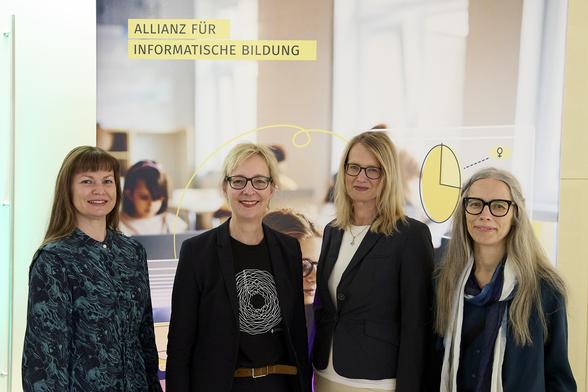 Elena Harwardt-Heinecke (Bereichsleitung Forschung und Qualitätsmanagement von Kinder forschen), GI-Präsidentin Christine Regitz, Beatrice Stübing (Bereichsleitung Kommunikation von Kinder forschen), Anne Lehmann (Referentin Online-Lernen von Kinder forschen) stehen vor einer Fotowand mit der Aufschrift "Allianz für informatische Bildung". Sie schauen lächelnd in die Kamera.