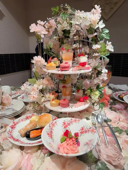 The table is adorned with floral decorations and an elegant display of pastel-colored treats including macarons, fruit tarts, and layered mousse. The overall ambiance is cozy and festive, perfect for a cheerful and intimate celebration.
