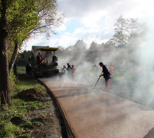 Bauarbeiter asphaltieren einen Geh- und Radweg und sind in Dampfschwaden gehüllt.