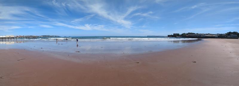 Ein Foto vom Strand und Meer. Ganz links und ganz rechts sind Häuser zu sehen.