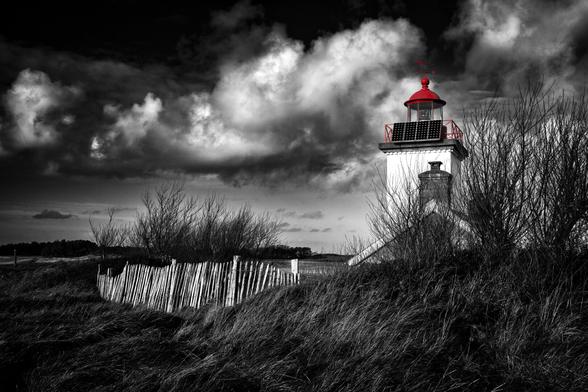 Schwarzweissfotografie mit Selektivfarbe Rot eines Leuchtturms in der Normandie.