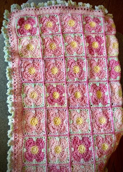 Crocheted baby blanket. Small yellow centers of varying pink 4 petal flowers made in squares and then joined all together with a green ruffle border.