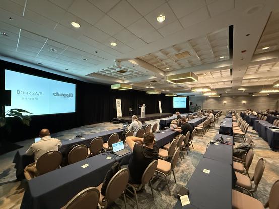 A large meeting room with rows of tables and chairs along with screens and lecturns and the usual meeting stuff