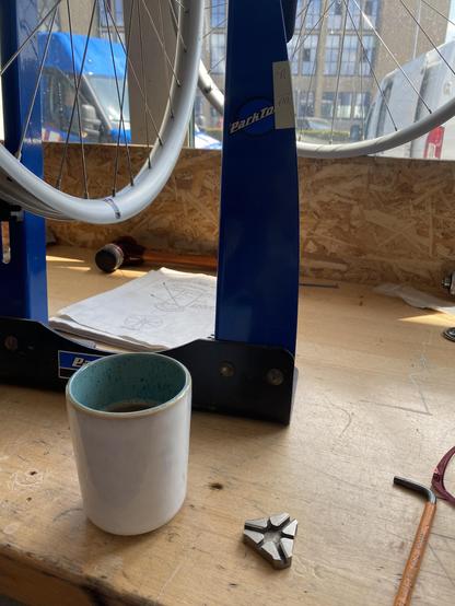 A cup of coffee next to a wheel trueing jig on a wooden workbench