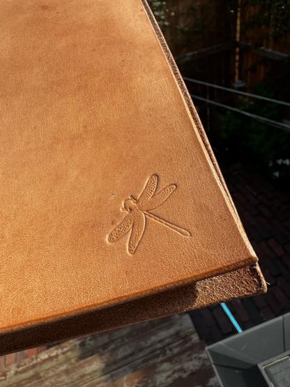 An amber brown leather journal cover, close up on the corner that contains a stamped dragonfly image.