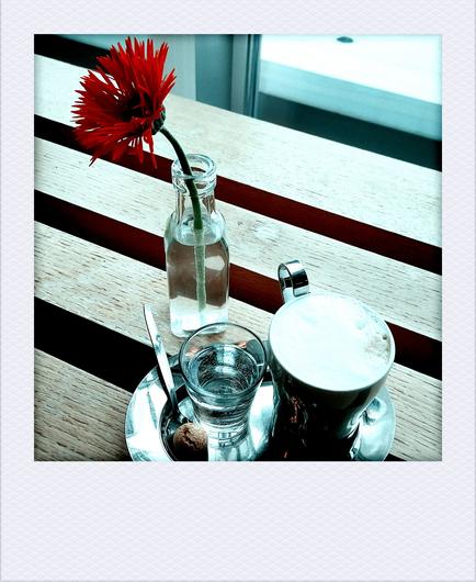 Blume, Kaffeetasse, Wasserglas auf einem Tablett auf Holzbalken.