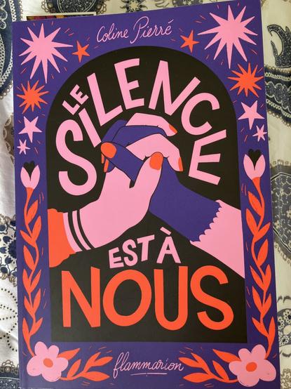 Couverture très colorée mauve et rose du roman de Coline Pierré, Le silence est à nous, deux mains aux ongles vernis dont les doigts s’entrecroisent pour marquer une solidarité forte, et des étoiles !