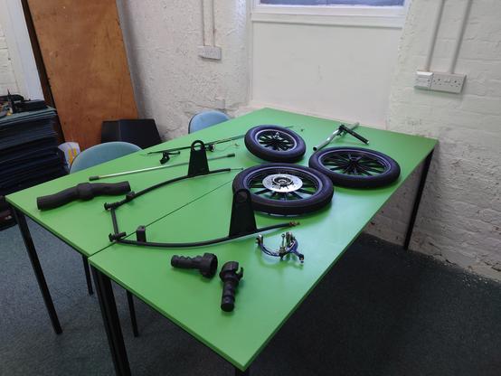 A picture of several Sinclair C5 parts, wheels, rear frame, handlebars, grips and brakes, spread across on a green table.