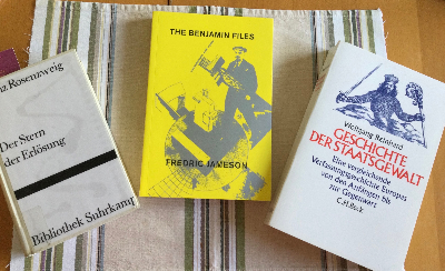 Auf einem Tischset liegen drei Bücher. Ganz links von Franz Rosenzweig Der Stern der Erlösung. Es ist ein weißes Suhrkamp-Hardcover. In der Mitte liegt das Buch The Benjamin Files von Frederic Jameson. Es ist ein gelbes Taschenbuch. Auf dem Titel eine konstruktivistische Collage von Gustav Klutsis aus den 20er Jahren, mit dem voranschreitenden Lenin, der einen Strommast trägt. Ganz rechts liegt Die Geschichte der Staatsgewalt von Wolfgang Reinhard. Es ist ein sehr dickes Taschenbuch mit hellem Creme-farbenen Einband. Über dem Titel sieht man die Staatsallegorie von Hobbes: über einer hügeligen Landschaft erhebt sich eine riesiger Koloss von König, mit Krone, Schwert und Szepter. Sein Leib besteht aus ganz vielen kleinen Menschlein.