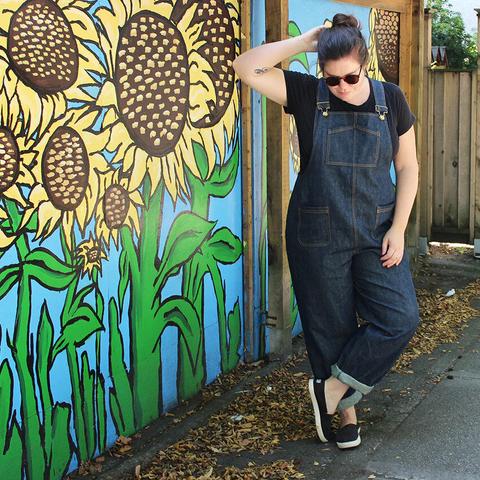 Helen wears dark wash overalls and a black top.
