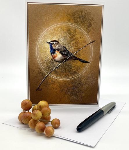 Photograph of an illustrated greeting card featuring a bluethroat bird, arranged with gold berries and a fountain pen.