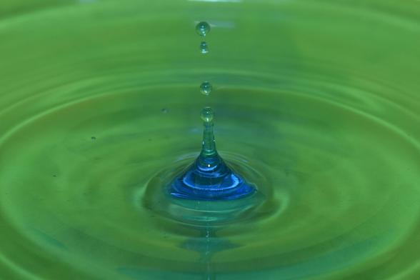 aufsteigender Wasserkegel in blau-grün mit mehreren fallenden Tropfen darüber vor grünem Hintergrund