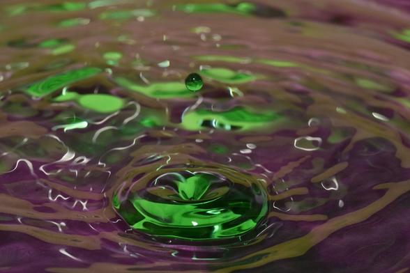 ein grüner Tropfen fällt auf eine donut-förmige grüne Welle in dunkelpinker Umgebung.