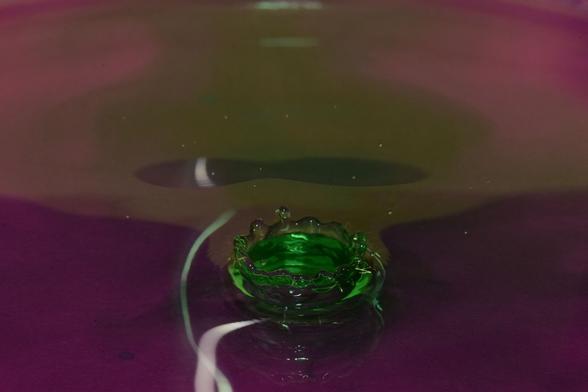 eine grüne Wasserkrone in dunkelpinker Umgebung, darüber ein grünlicher Bereich und links daneben verzerrte Lichtspiegelungen