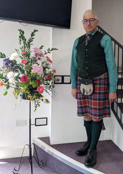 Me dressed in a kilt and semi-dress sporran next to a spray of flowers on a stand.