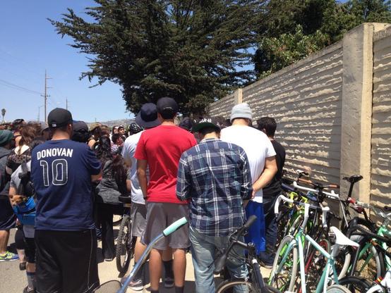 Mourners are gathered near a collision site on July 12, 2014. They  are standing along a wall where a temporary ghost bike would be placed, later to be replaced by a memorial mural. Many came by bicycle, and some bikes are visible in the photo.