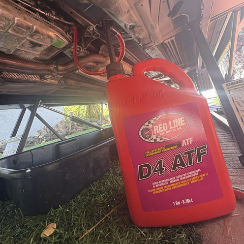 A red gallon jug of automatic transmission fluid sits on the ground underneath my 2003 BMW 530iT, which is up on QuickJack lifts. A hose with a hand pump runs from the mouth of the transmission fluid bottle into the fill hole on the side of the ZF 5HP19 automatic transmission.