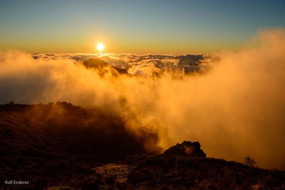 A golden sunset illuminating fluffy clouds and mountainous terrain, creating a serene and atmospheric landscape.