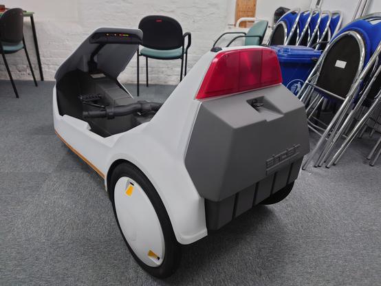 A rear side view of the Sinclair C5 fully assembled and cleaned, the POD LEDs are lit up, sitting on a carpeted floor.