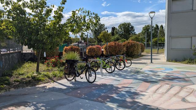 Aparcabicis junto a la Casa de la Juventud de Parla, hay cuatro ciclos estacionados sobre una losa de hormigón, atados a los aparcabicis. Justo detrás hay un poco de vegetación.