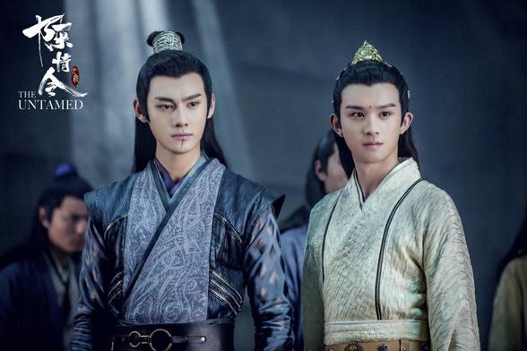 Image focusing on Jiang Cheng and Jin Ling. Uncle and nephew are standing side by side with similar stances and body language, and both looking toward the same offscreen target being 9 the right side of the image. Jiang Cheng has a faint vertical trail of blood below his mouth.