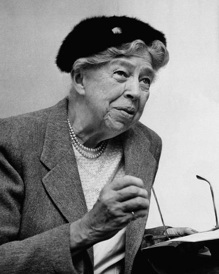Black and white photo of 1st lady Eleanor Roosevelt. She is wearing a blazer and cap while speaking at a lecturn.
