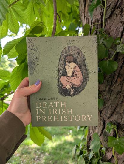 Holding the book "Death in Irish Prehistory" by Gabriel Cooney in front of a tree