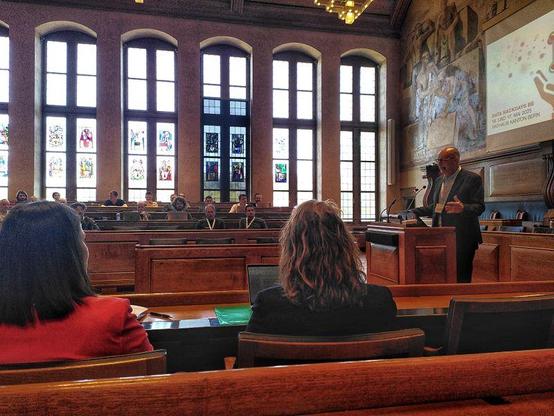 A speaker (André G.) in front of a political assembly in a historic government building
